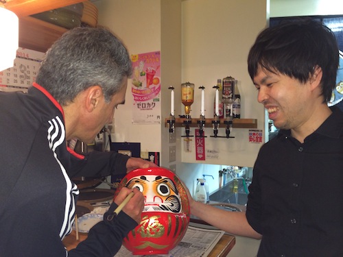 Art Azarbarzin, GPM project manager, fills in the second eye of the JAXA Daruma doll at the party after launch with JAXA engineer Hyakusoku Yasutoshi, Feb 28. Credit: Lynette Marbley