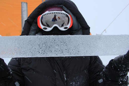 Lora with Clem reflected in goggles holding an ice core with water bubbles.
