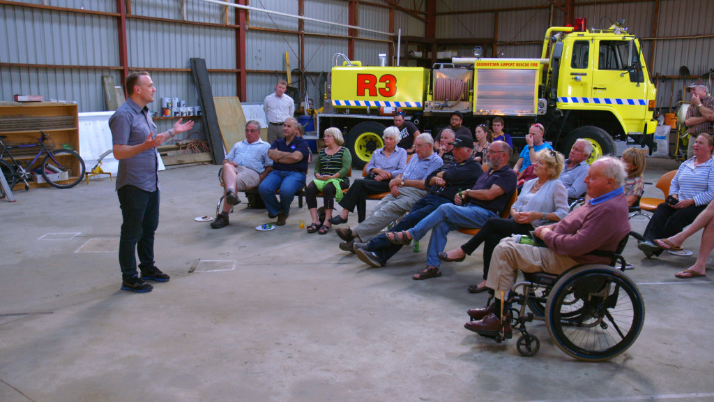 A group of people in a hanger listening to a presentation.
