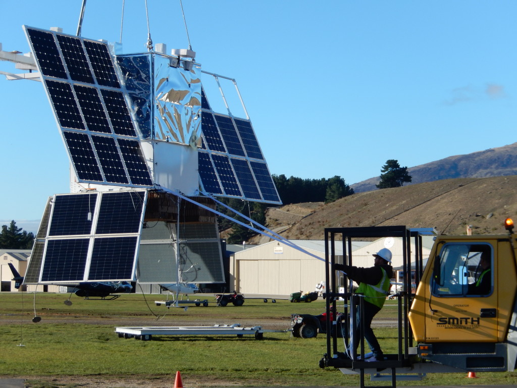 A payload hangs from a crane while a technician performs work.