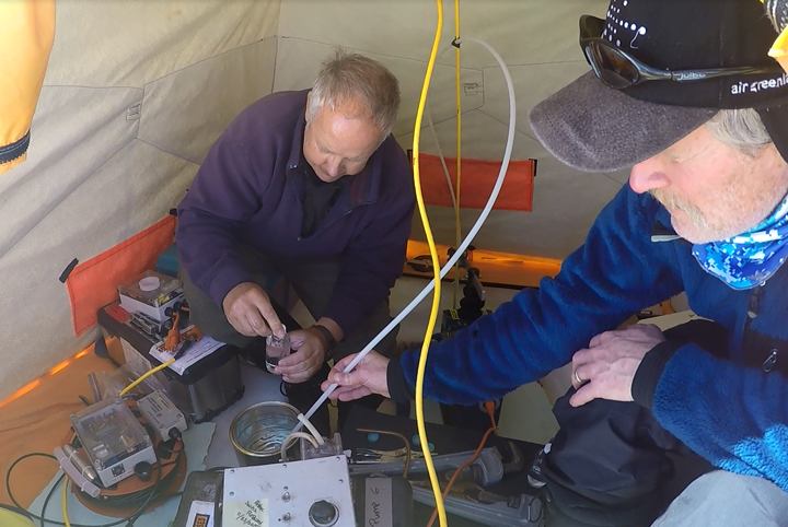 iWS standing next to the firn and water level logging station with our snowmobile in between for scale.