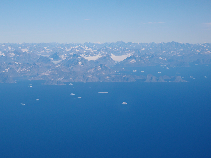 First view of the coast of East Greenland. The ocean is filled with enormous icebergs.