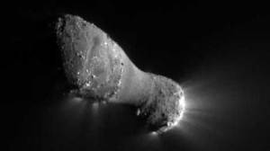 A close-up view of a peanut-shaped object with jets of material streaming out of the right end.