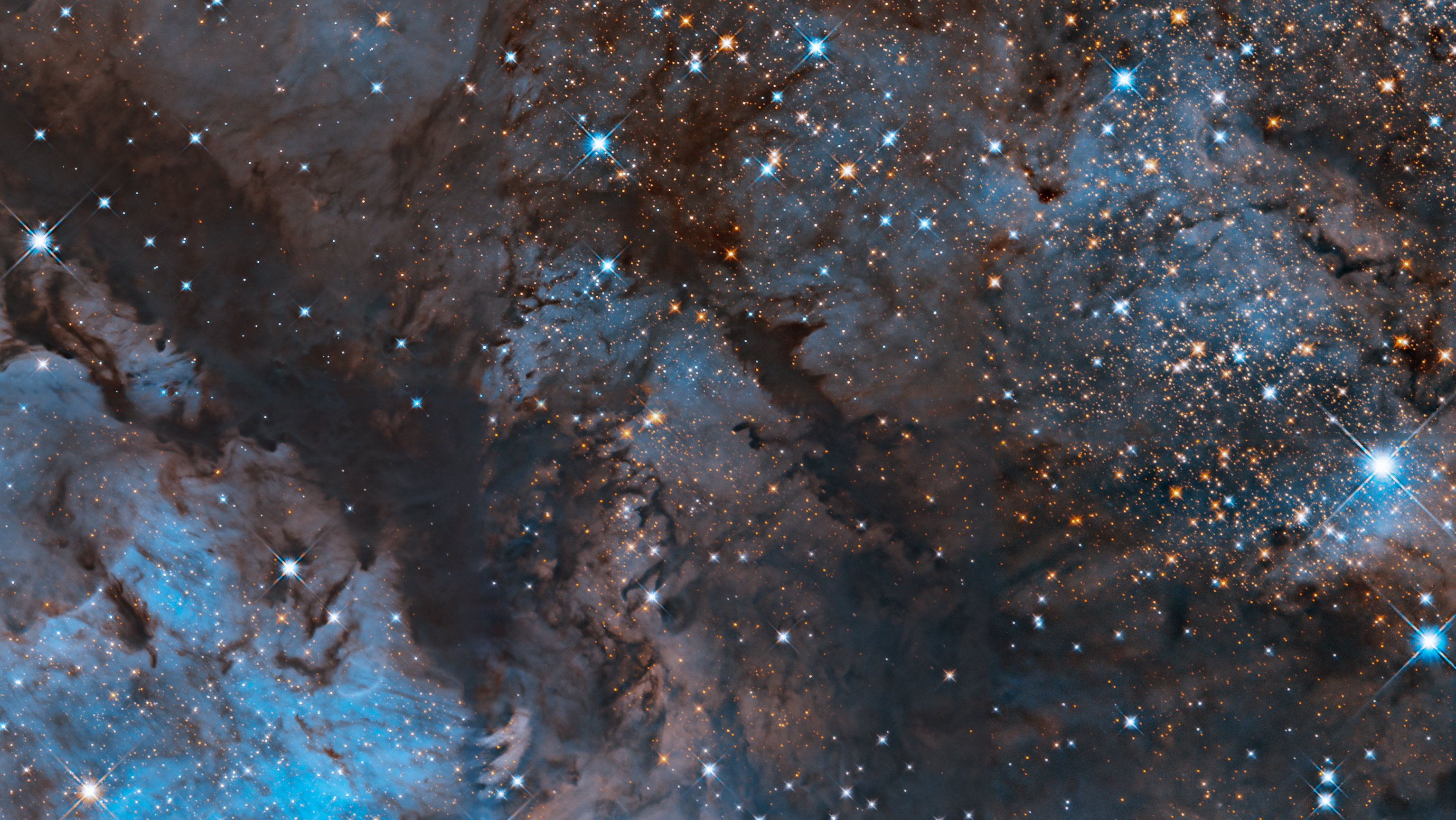 Blue and orange stars glitter across the image, interwoven with dark clouds of brown dust and bright, glowing regions of blue.