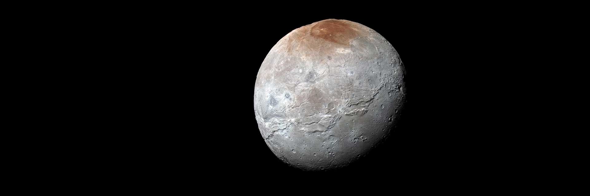 A full glove view of Pluton's moon, Charon. The moon is gray with a reddish cap.