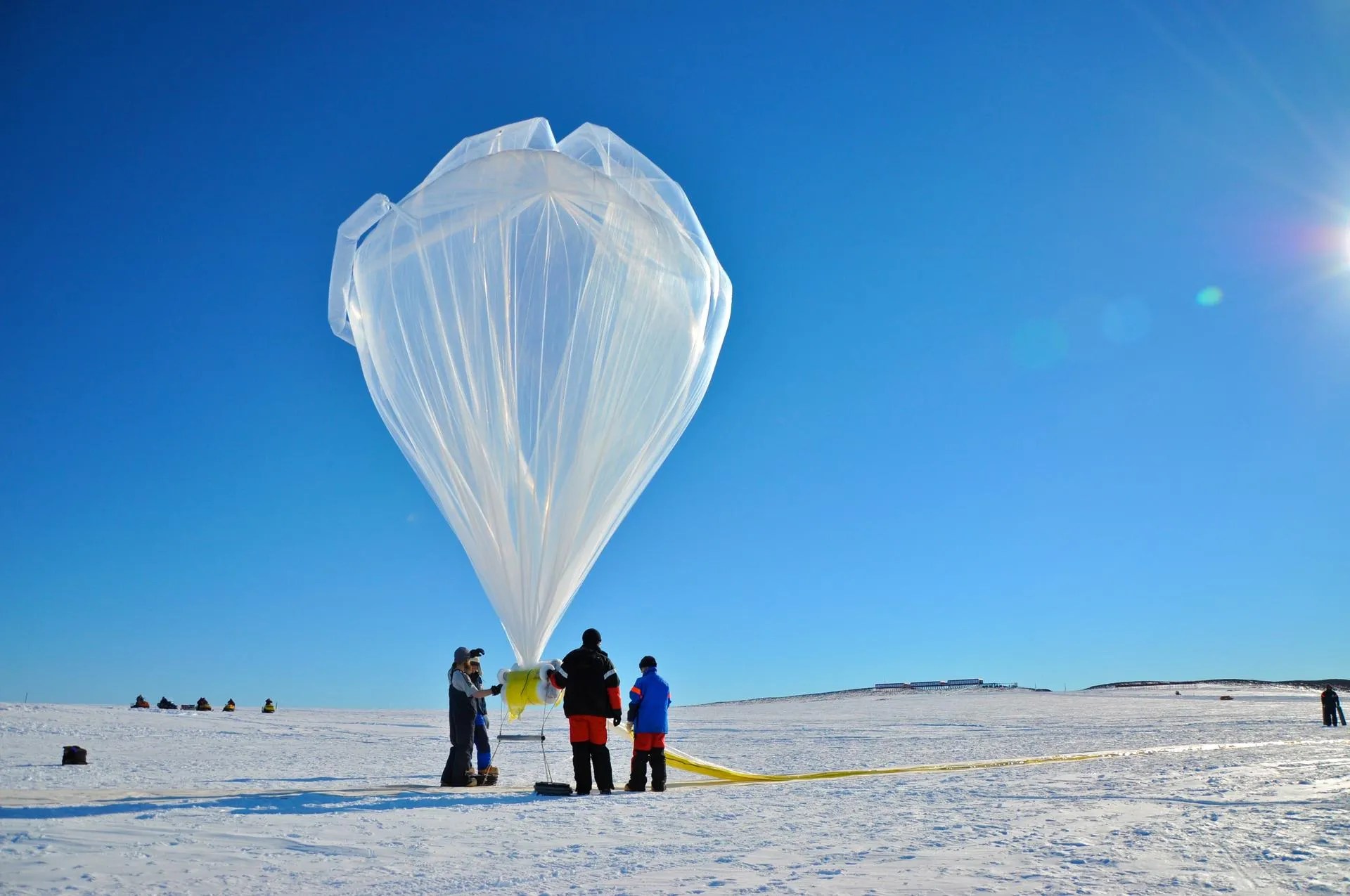 A large space weather balloon is surrounded by three people as it prepares for launch