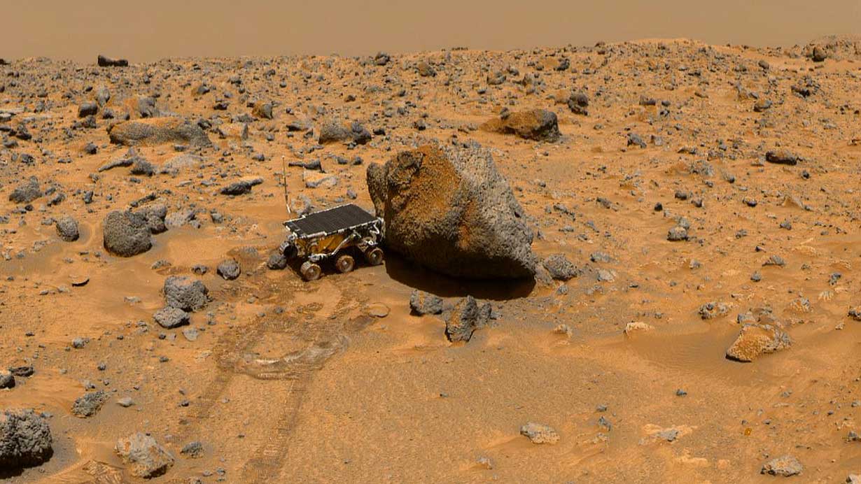 Small rover sitting against a rock on the red soil of Mars