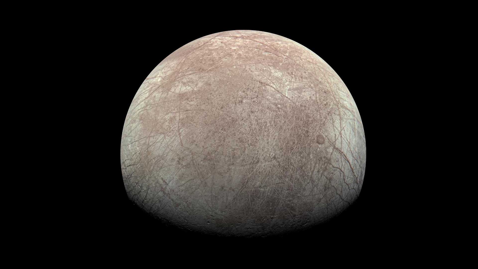 A view of Europa showing most of one side of the moon. The moon is gray with reddish bands running across it.