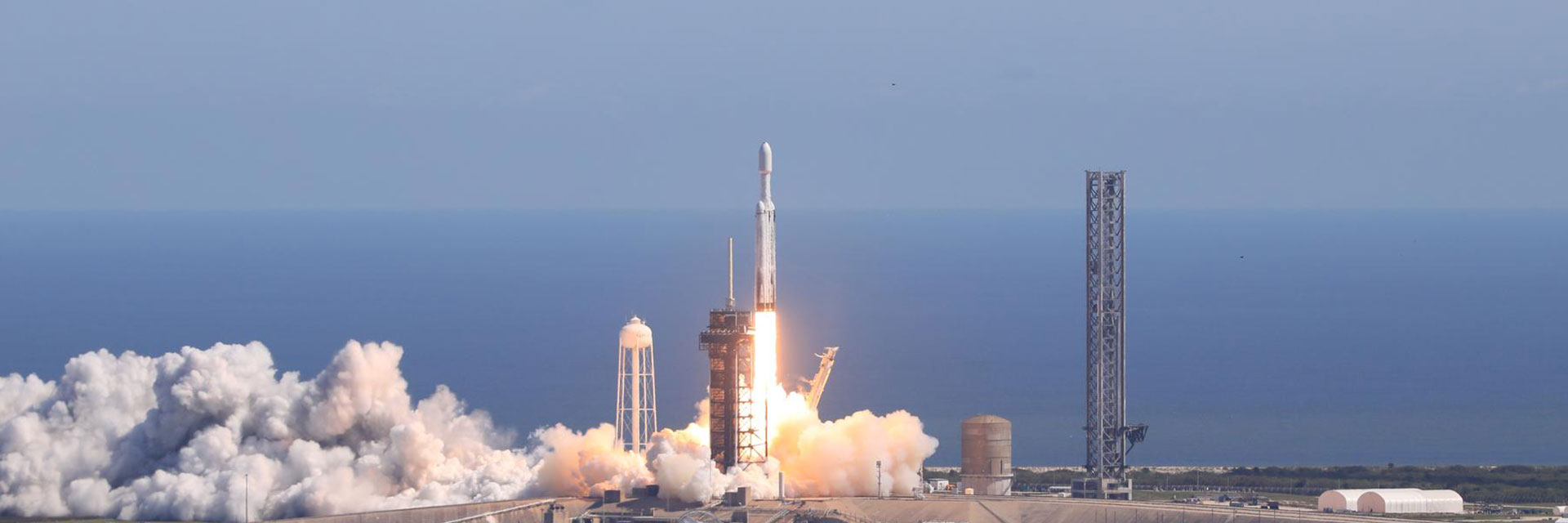 A white rocket with Europa Clipper on top in its protective fairing lifts off the launch bad with a trail of fire and white, billowy smoke below.