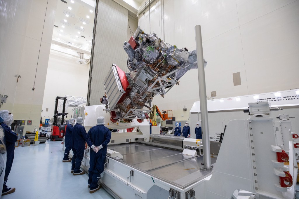 Workers in blue protective clothing and white head covers watch as Europa Clipper is lifted and rotated.