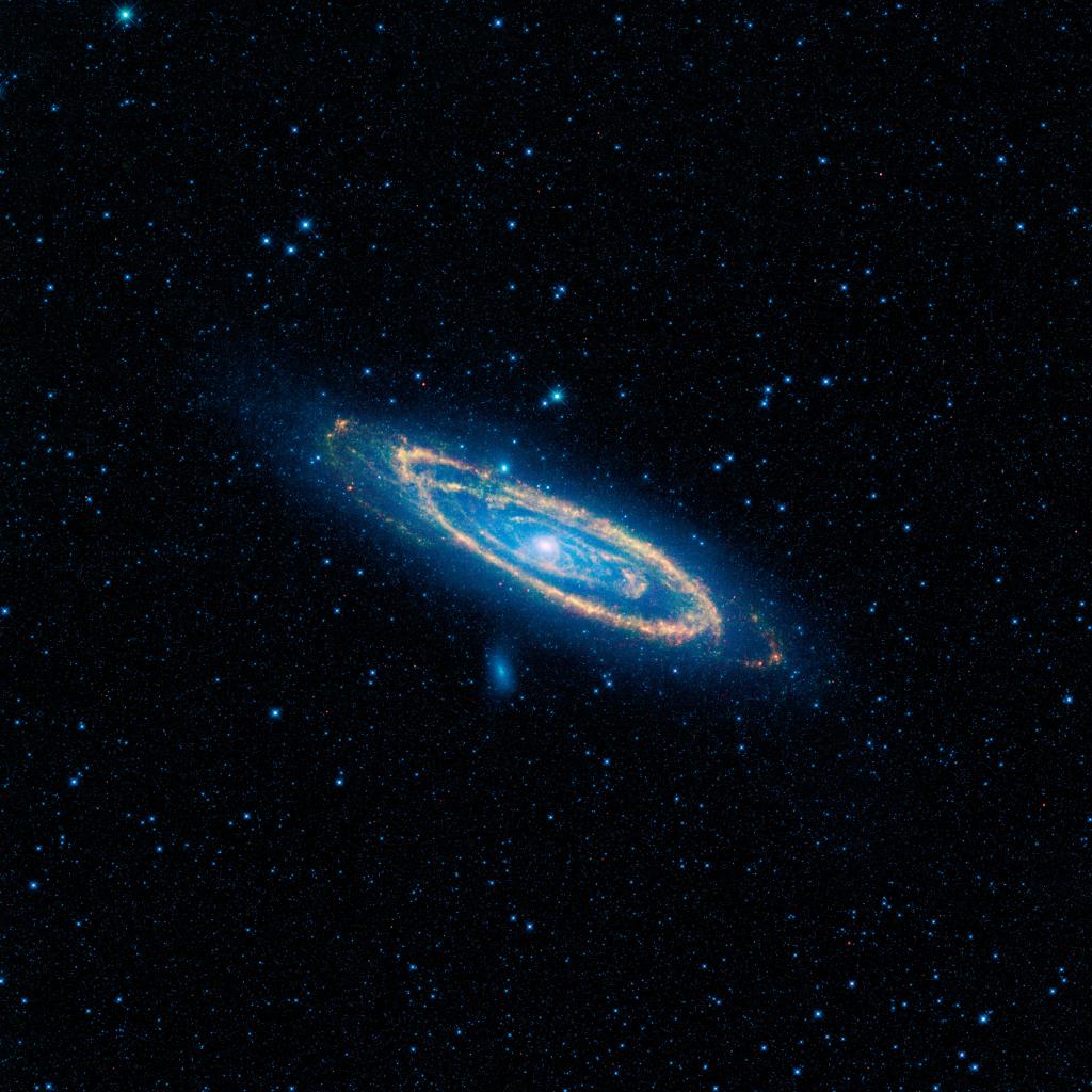 Against a black space backdrop speckled in blue pinpoints of starlight, a spiral galaxy sits in the center of the image, tilted from upper left to lower right, anchored at the center by a large dot of white light. Around that are swirling rings of very bright and light green and golden yellow, with the outermost ring looking like an oval of golden glitter glued to black velvet. A fainter oval made by an emerald green cloud sits just outside the glitter ring.