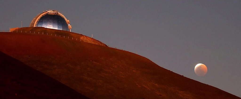 The domed telescope sits atop a red-orange hill at sunset