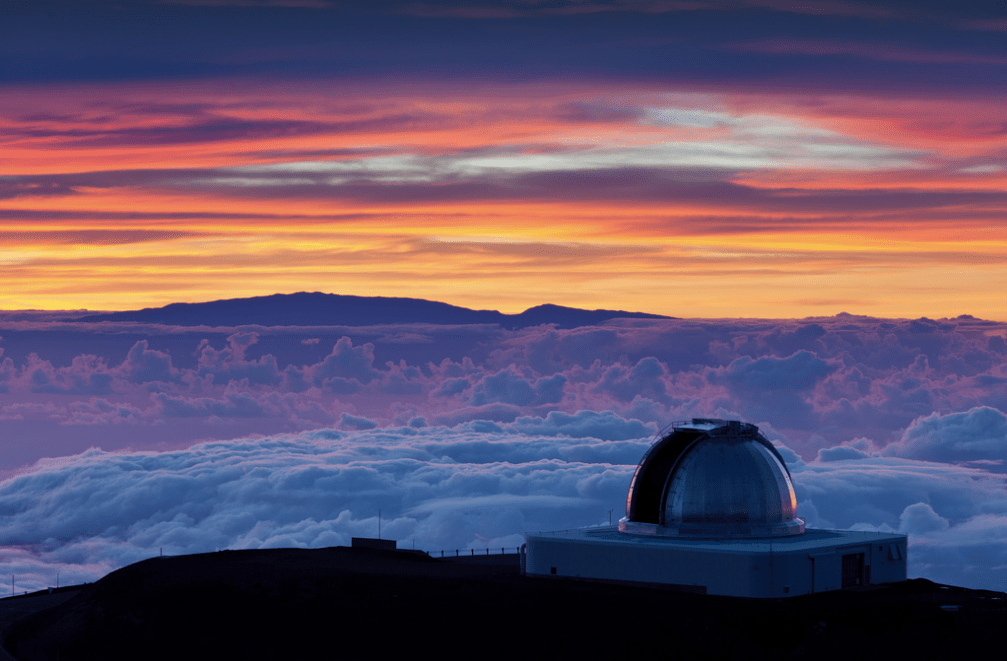 Orange and purple sunset sky with clouds below and domed telescope in the lower right corner