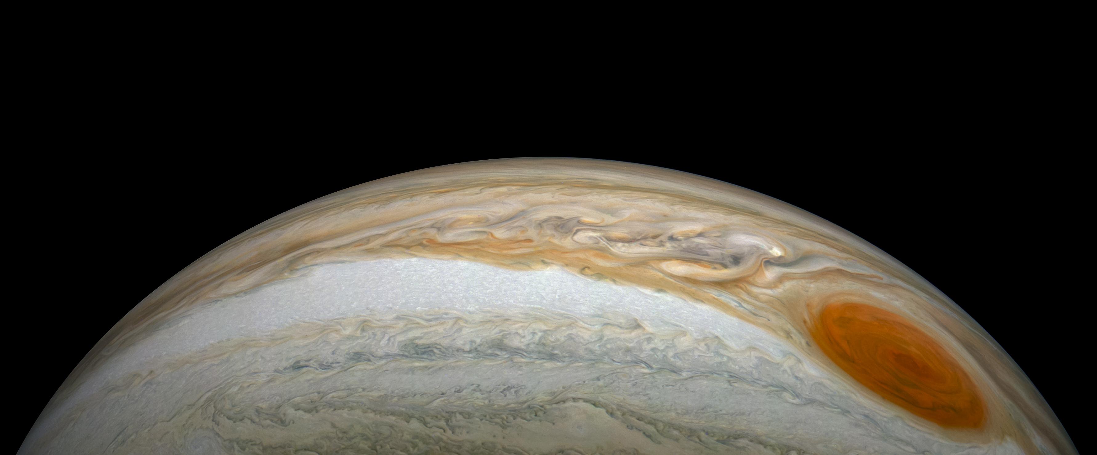 A crescent view of Jupiter with its bands of beige, and orange clouds. The Great Red Spot in the right, bottom corner.