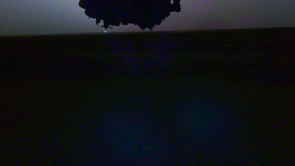 Part of the InSight Lander is visible just above the rising Sun on Mars