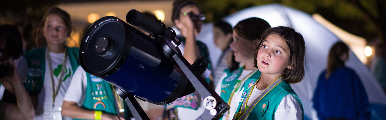 Photograph of a girl scout standing near a telescope