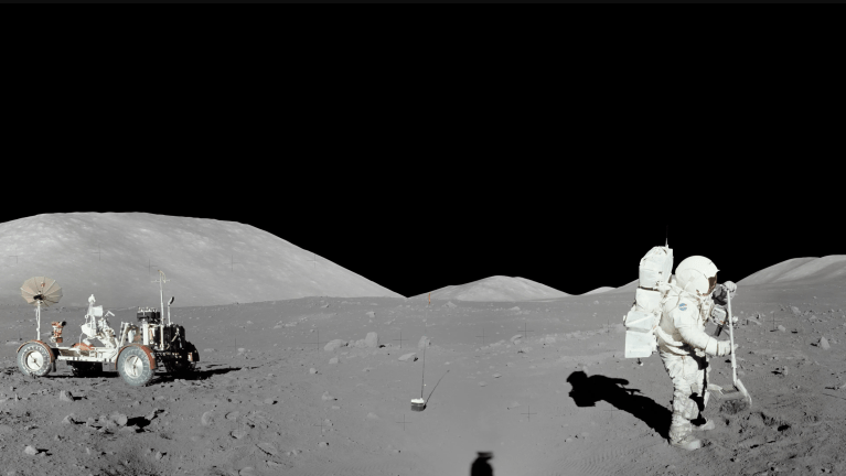 On the Moon, an astronaut holds a shovel, with a rover and stark hills in the background, under a black sky.