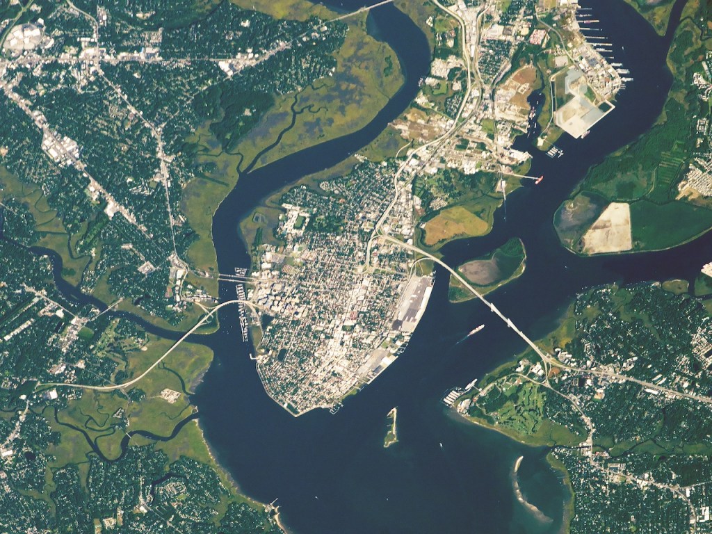 Satellite view of a peninsula between two relatively narrow rivers, with land visible on each side. The rivers meet at the point. The human settlement in the region is primarily on the peninsula, but another notable grouping is in the upper left.