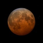 Eclipsed Moon, in a dark orange shadow gradient deepest towards the bottom of the image.