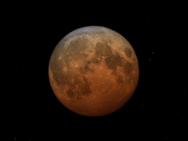 Eclipsed Moon, in a dark orange shadow gradient deepest towards the bottom of the image.