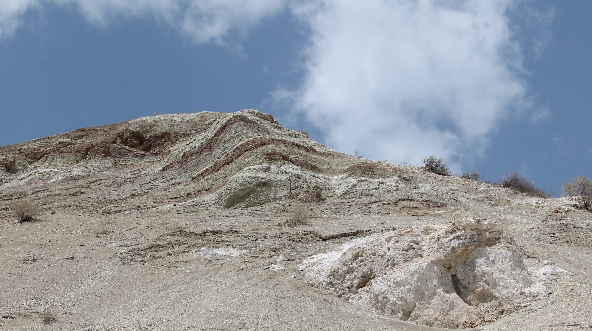 Rocky outcrop in a sandy, hilly area, under a blue sky with a cloud.