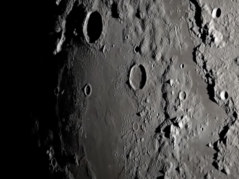 Close-up view of the transition between light and shadow on the Moon, with craters and ridges dramatically illuminated from the right.