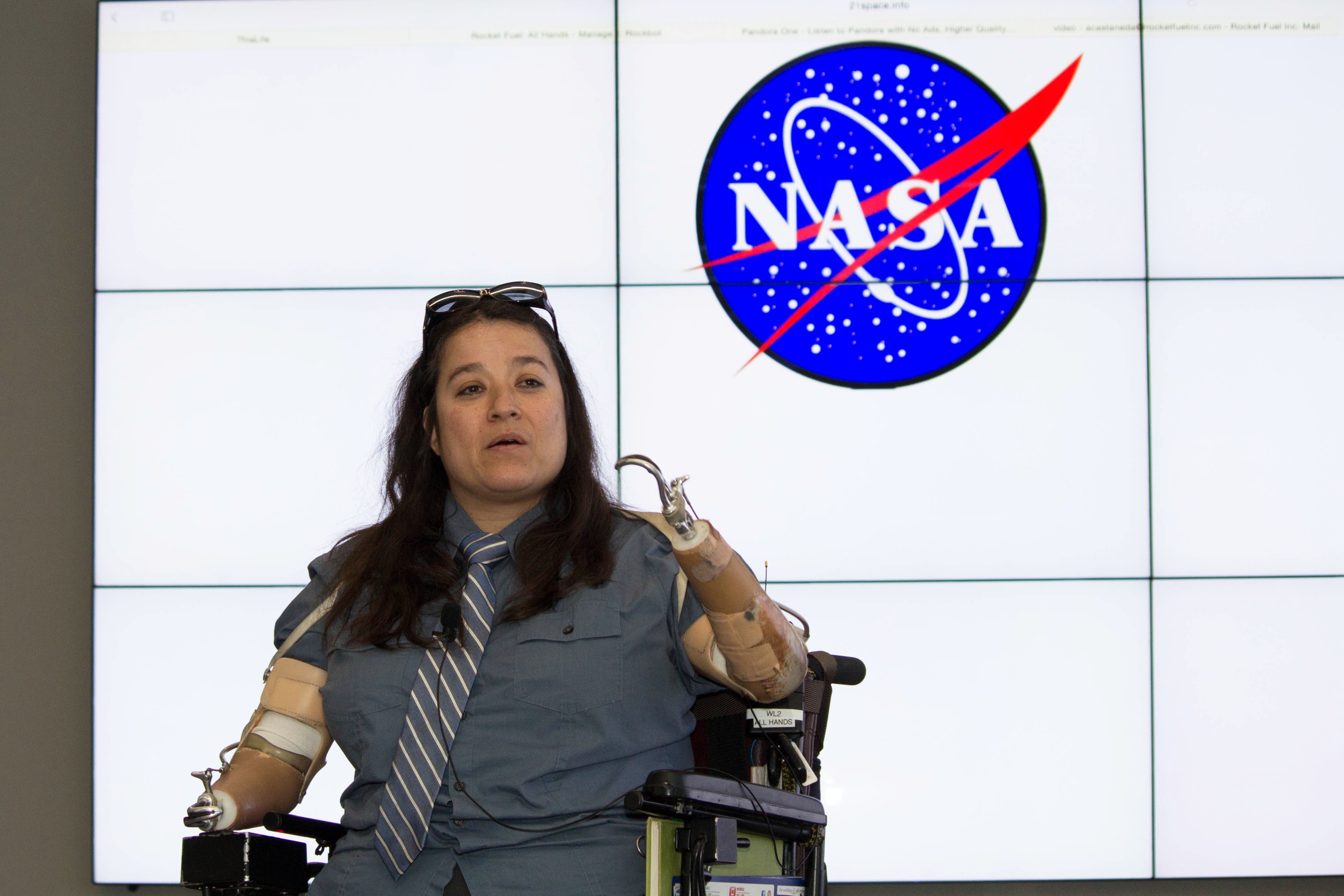 Dana Bolles speaking from her motorized wheelchair in front of a NASA logo.