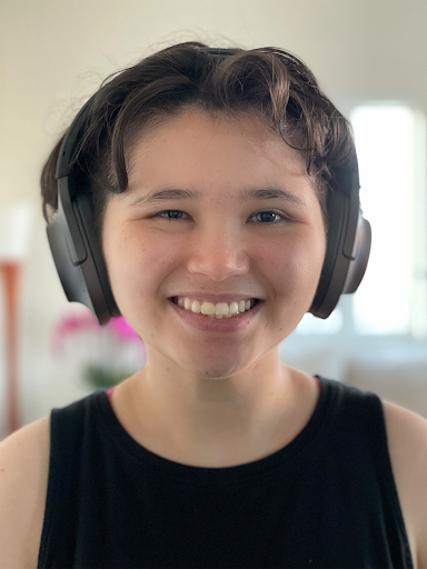 a close-up of a young person smiling while wearing over-ear headphones. They have short, dark, wavy hair and a warm expression