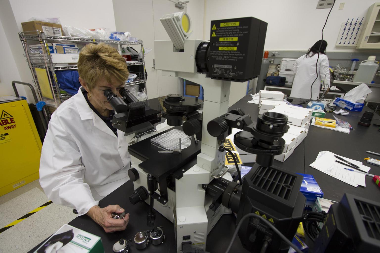 A scientist in a white coat looks through a microscope.