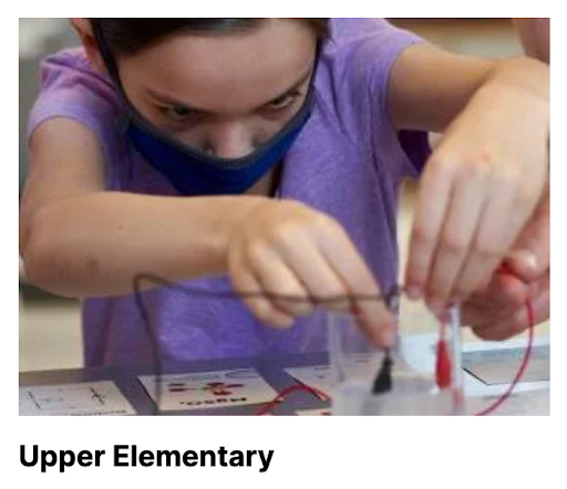 Student wearing a mask holds two electrodes in a beaker of water.