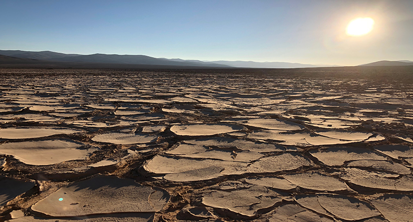 Dried, cracked land in the lower third of the image, with the Sun blazing down from the upper right