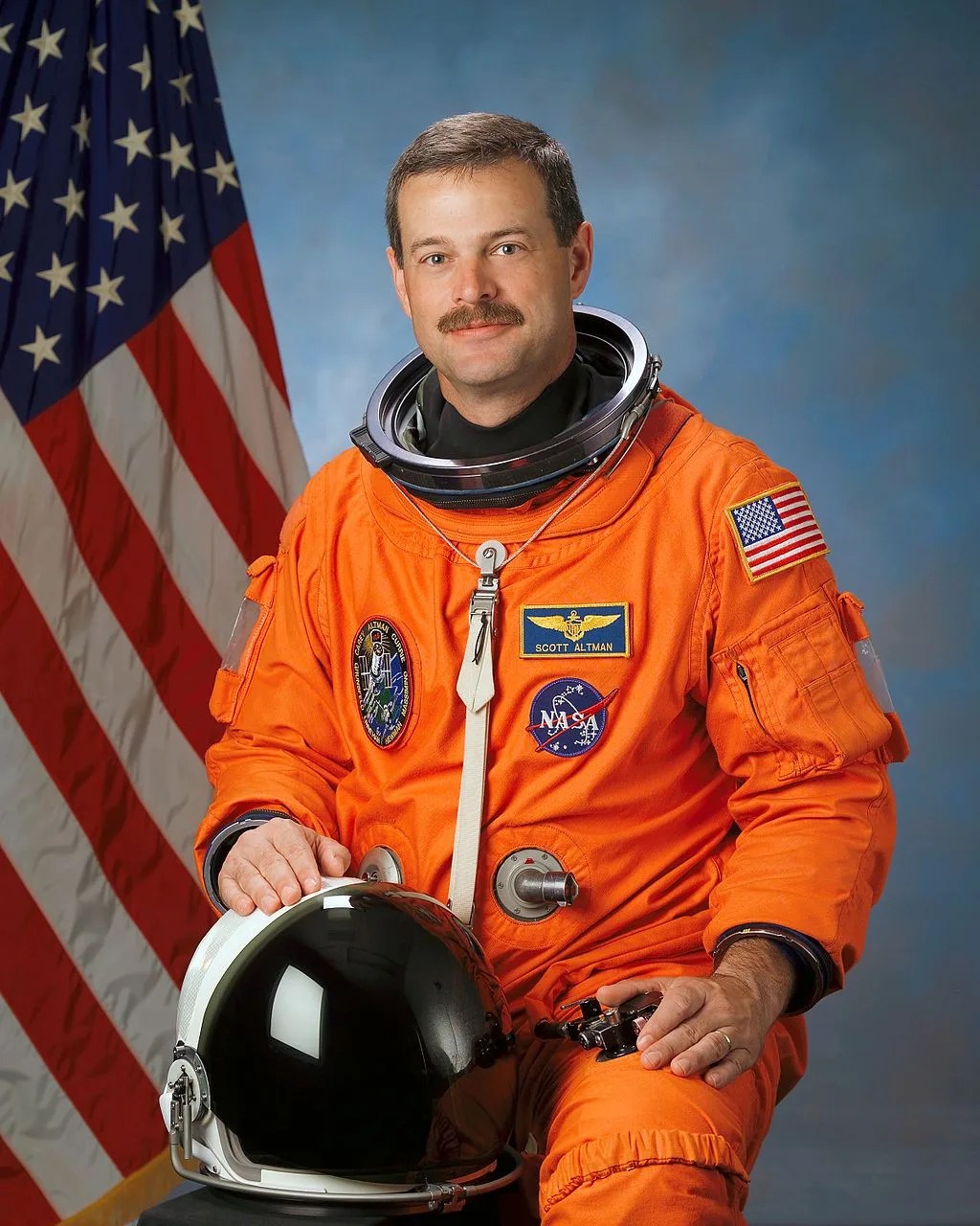 Photo of astronaut Scott Altman in his orange spacesuit. American flag is behind him.