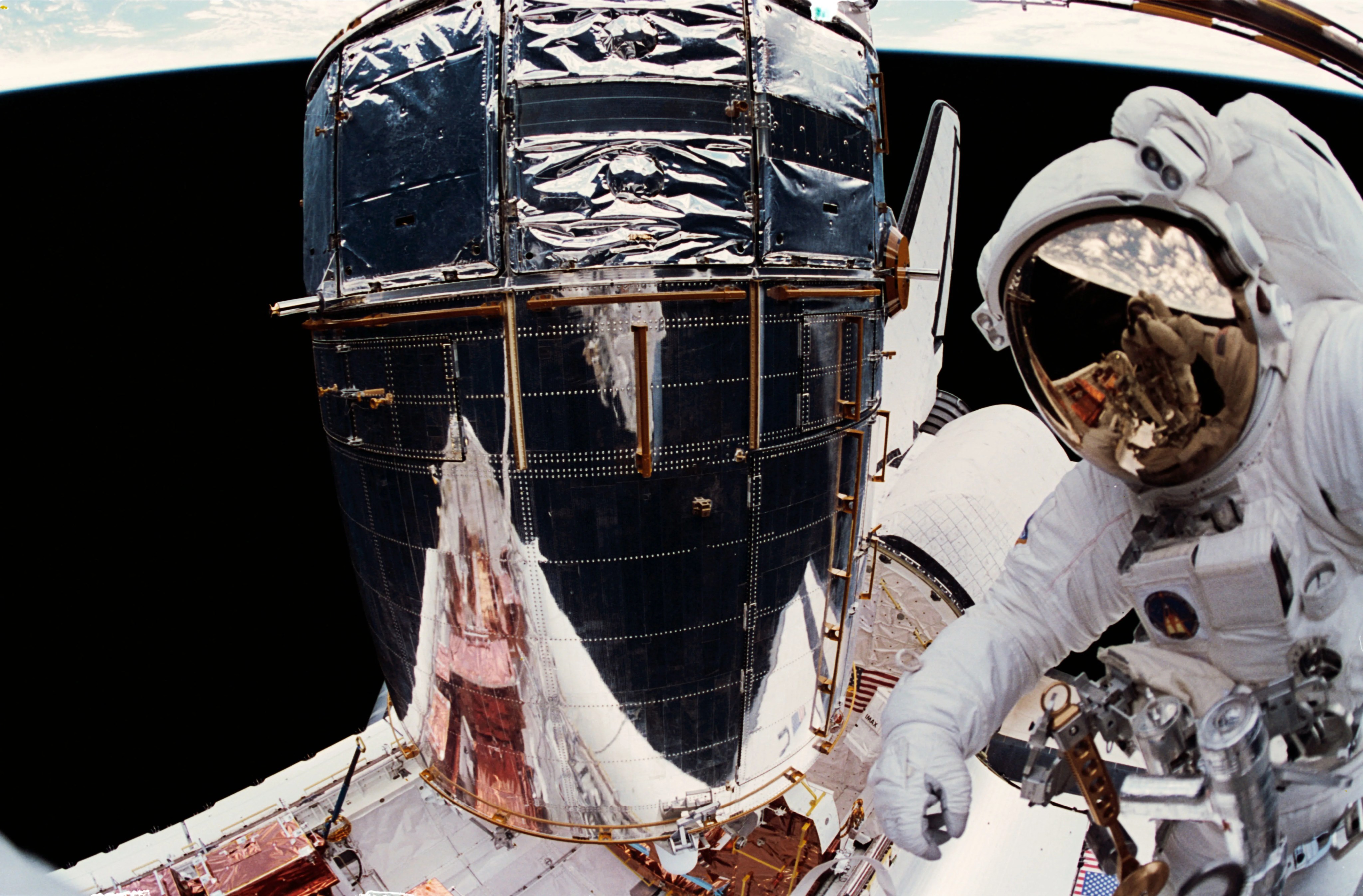 Astronaut in a white space suit in space taking a selfie with Hubble in the photo.