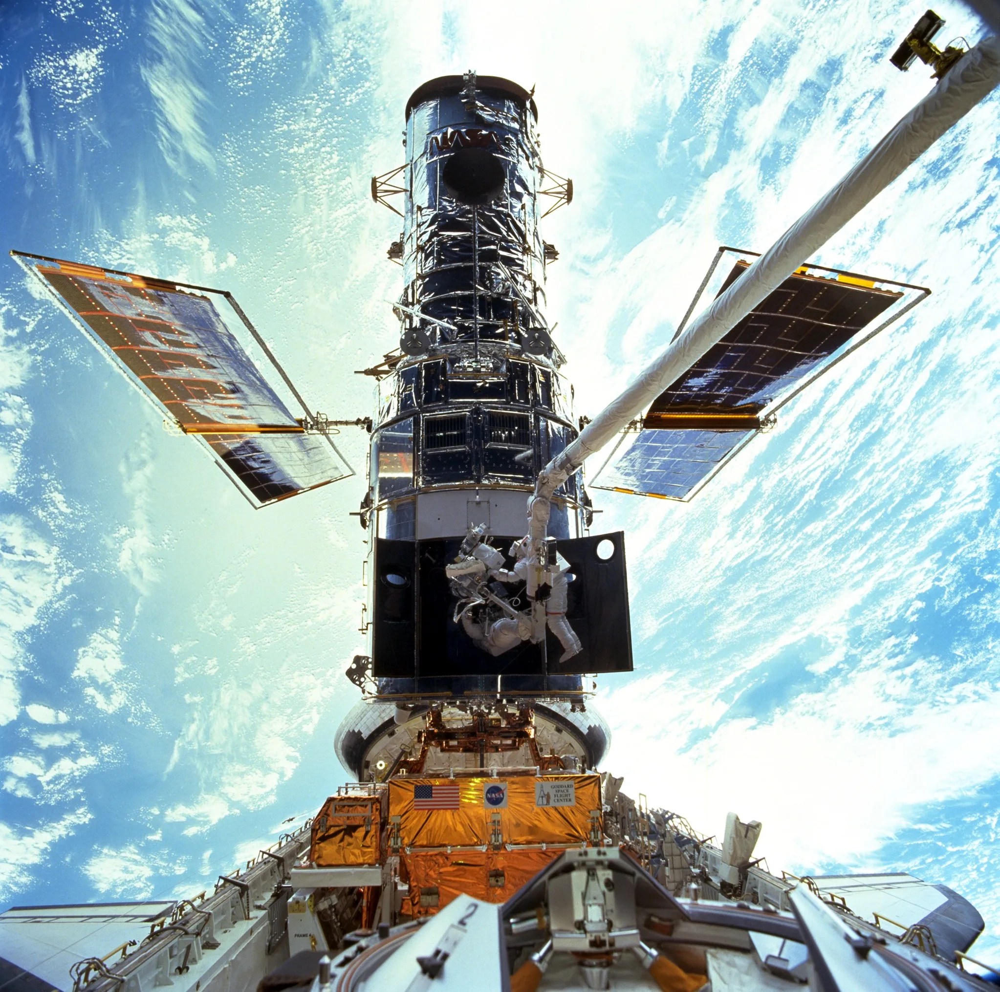 Two astronauts work inside the bottom of Hubble while flying over the earth.