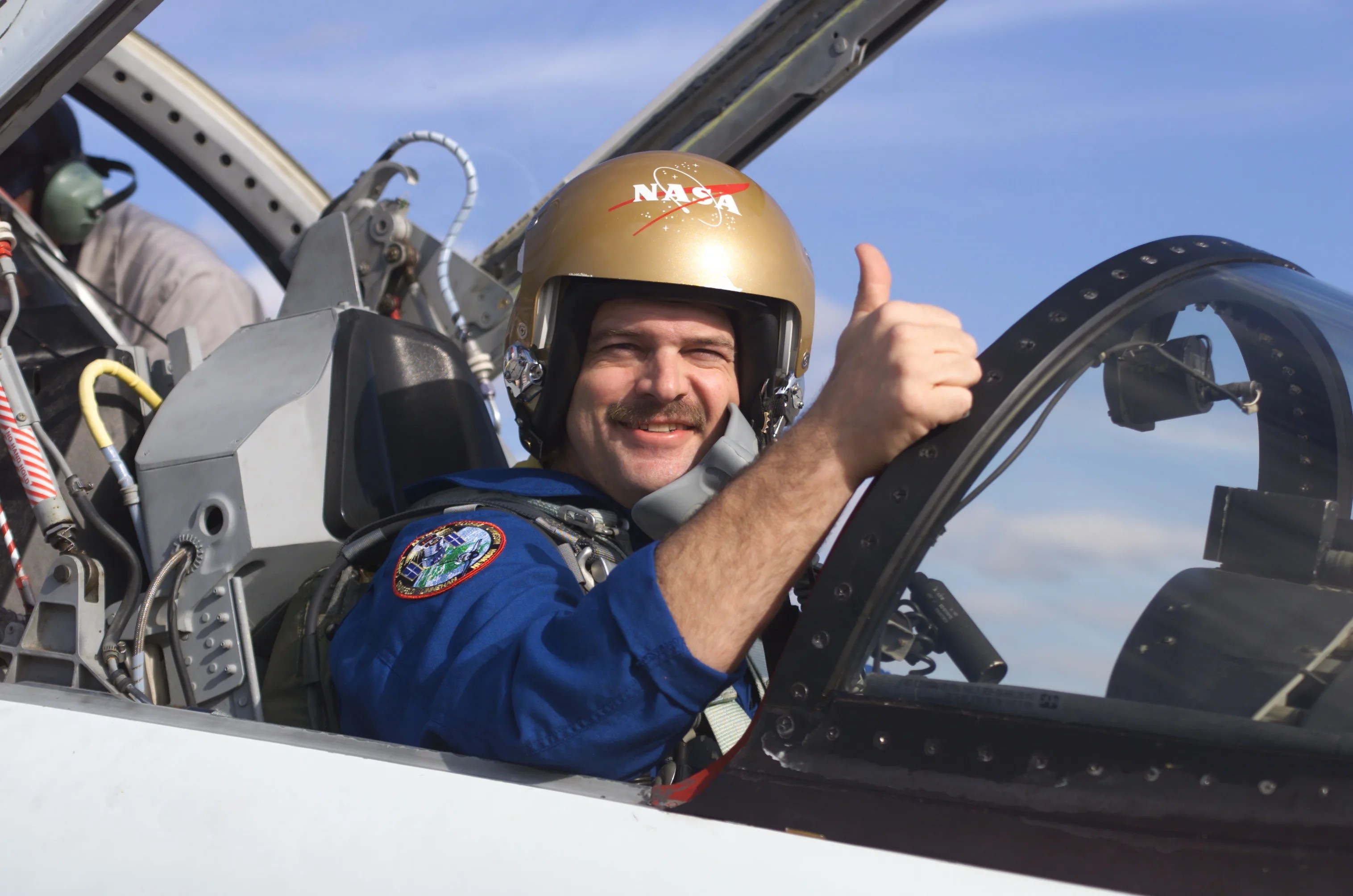 Astronaut Scott Altman sits in the cockpit of a plane, shooting a thumbs-up to the camera.