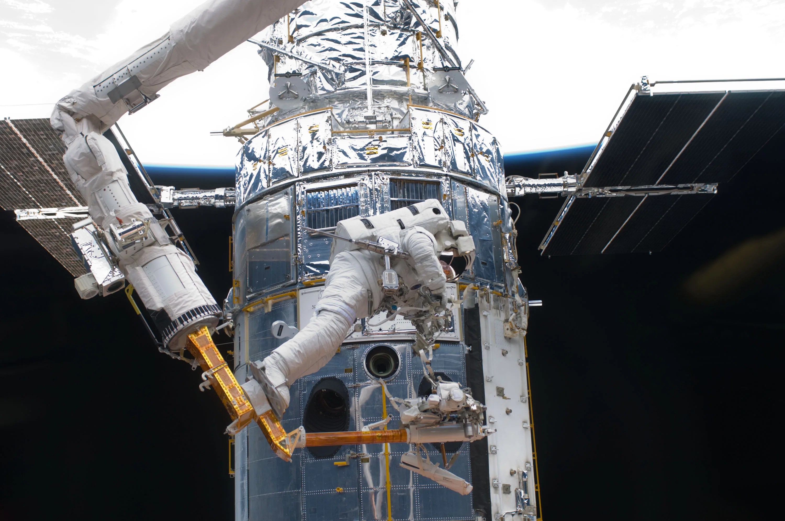 Using a robotic arm, an astronaut does maintenance work on Hubble. In the top third of the picture, Earth is seen in the background.