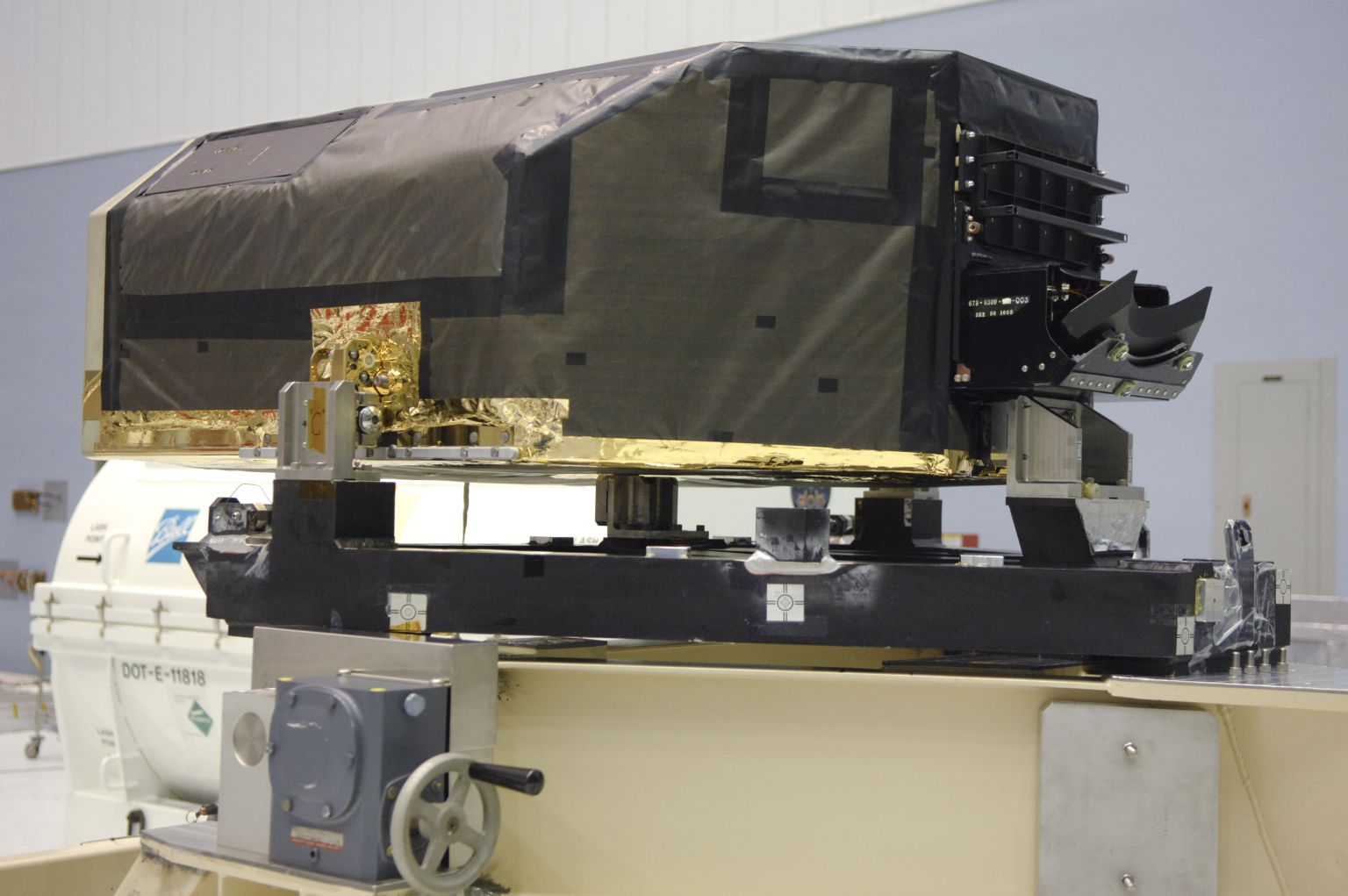 A large black box with tapered sides and edges, that is a Hubble Fine Guidance Sensor, sits in a cleanroom