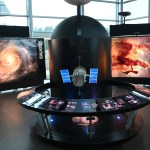 A model of Hubble sits in the middle of a round station with a backlit semi-circle panel describing the spacecraft and the mission's history