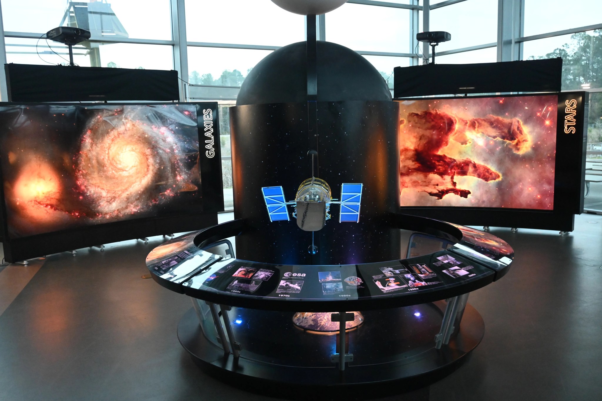 A model of Hubble sits in the middle of a round station with a backlit semi-circle panel describing the spacecraft and the mission's history