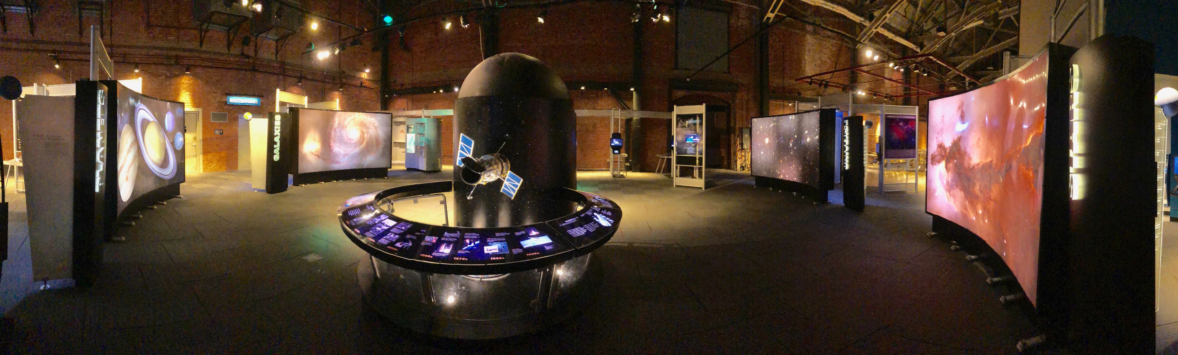 A panorama view of the Hubble traveling exhibit with its center piece model and four science stations.