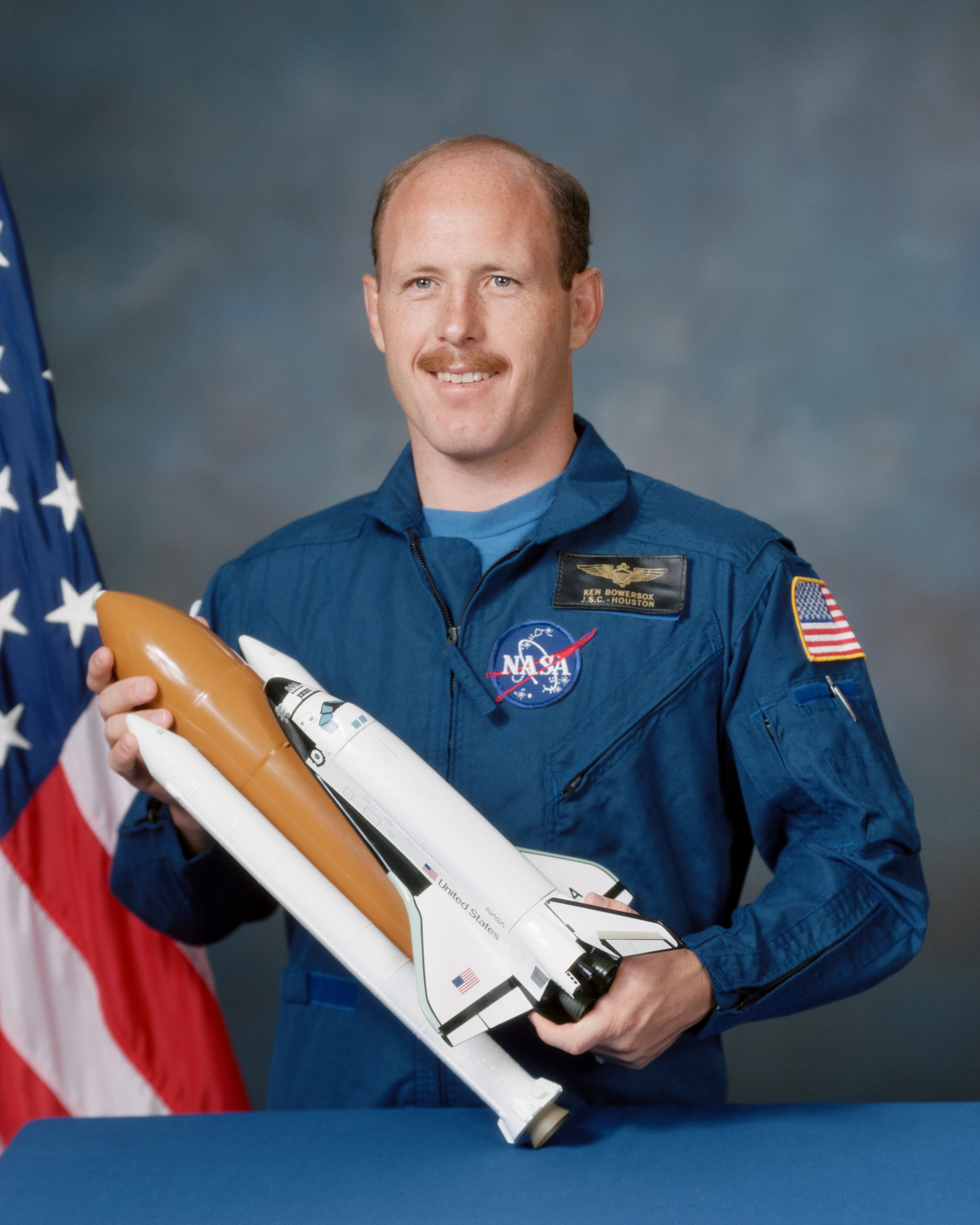 Astronaut Kenneth Bowersox, in his official portrait, holding a model of the space shuttle Discovery.