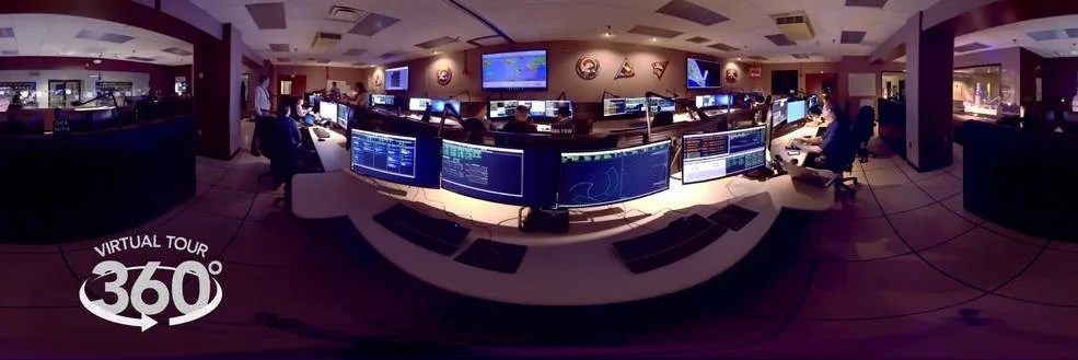 360 image of Hubble's "Space Telescope Operations Control Center" The image is stretched because it is designed for 360 degree viewing. The image shows many desks within the control center with data on their screens.