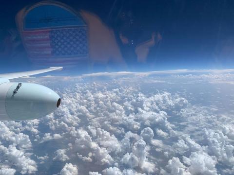 View out of the cockpit of the ER-2 cockpit while in flight. The view looks down on fluffly clouds below and the deep blue sky is above.