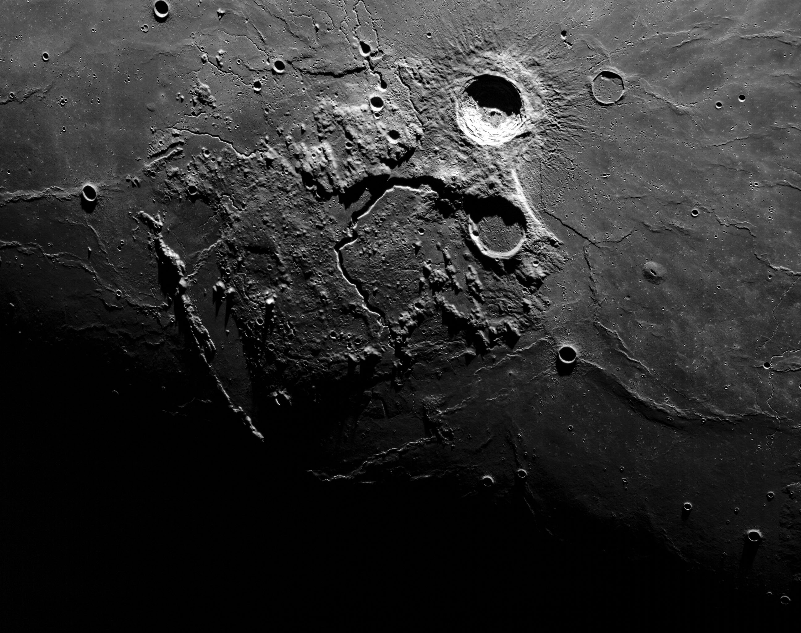 A beatuiful close image of some craters on the lunar surface taken by the Artemis I crew. The top of the photo is lit by the sun and it slowly fades to darkness at the bottom.
