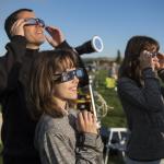 Three people stand, wearing eclipse glasses, smiling.