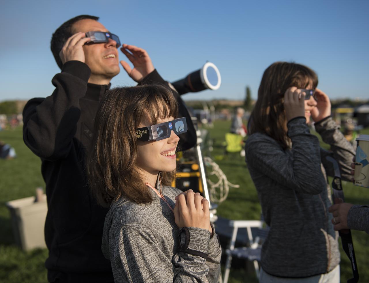 Three people stand, wearing eclipse glasses, smiling.