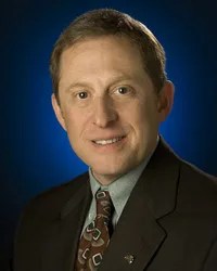 Portrait of astronomer Alan Stern in a black suit set against a blue background