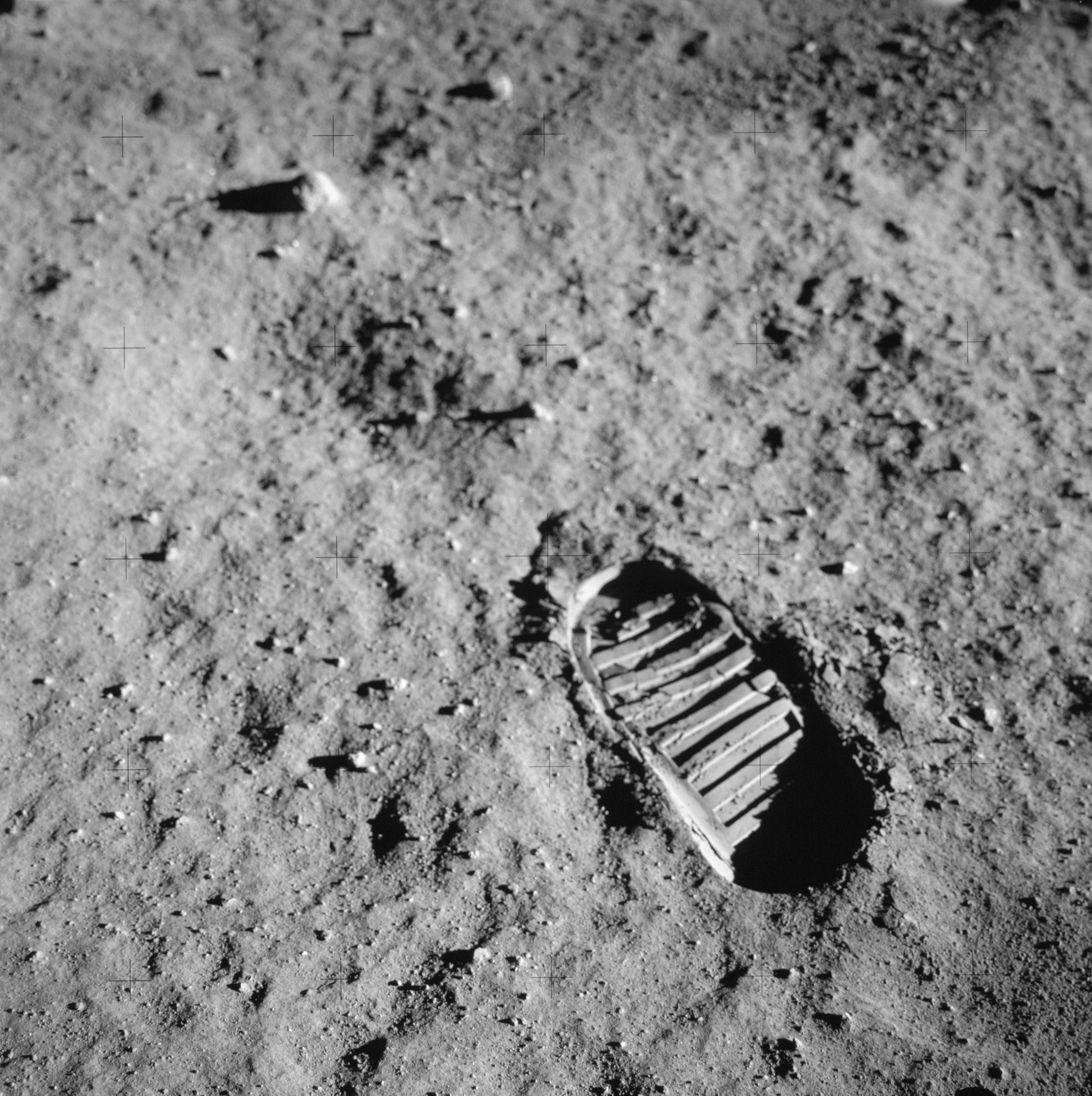 A striped bootprint is pressed into the powdery lunar soil.