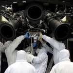 Six people in white clean suits work on the underside of a replica of Hubble.