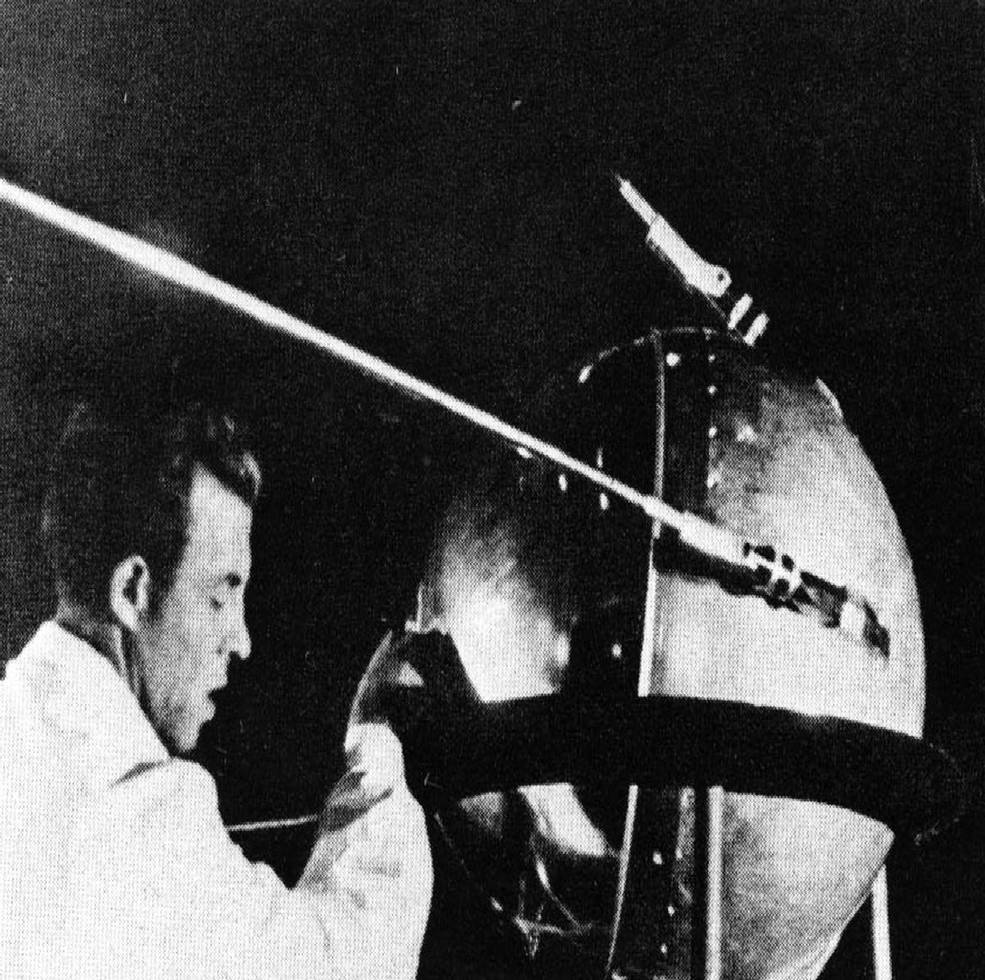 Black and white image of Sputnik 1 with a man standing on the left working on the satellite.